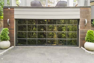Modern garage with large glass doors, surrounded by landscaping, offering a bright entrance to your home.