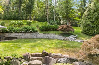 Lush, landscaped backyard features tiered greenery, stone walls, and a tranquil space for outdoor gatherings.