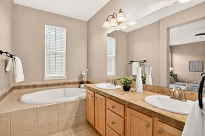 Spacious bathroom featuring dual sinks, a relaxing tub, and natural light from large windows.