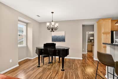 Bright open space features a grand piano, ample natural light, and a seamless flow to the kitchen.