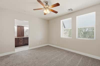 Spacious primary suite with plush carpeting, large windows, and a ceiling fan for added comfort. Designed to provide a peaceful retreat at the end of the day.