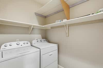 Functional laundry room with built-in shelving and included appliances. Convenient upstairs location helps streamline household tasks while offering practical storage solutions.