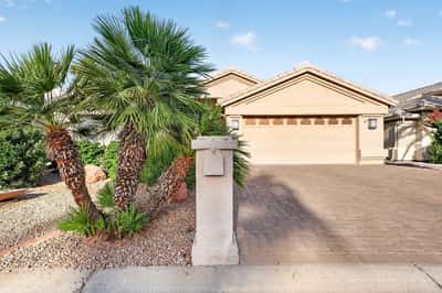 Tropical-inspired palm trees and manicured desert landscaping create a striking first impression. The home's clean exterior lines and paver driveway contribute to its move-in ready presentation.
