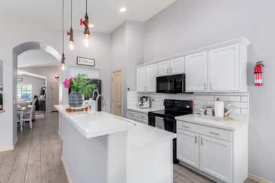 Featuring quartz countertops, subway tile backsplash, white cabinetry, pendant lighting, and generous prep space, this bright kitchen blends timeless style with everyday functionality.