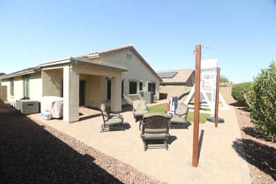 A covered patio overlooks the spacious backyard featuring paver hardscaping, low-maintenance landscaping, and artificial turf. Designed for comfortable outdoor enjoyment throughout the year.
