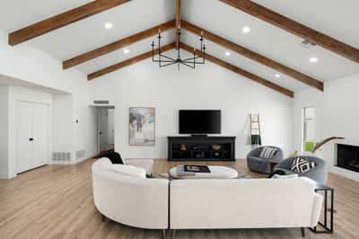 Vaulted ceilings, exposed beams, expansive windows, and beautiful flooring define this sophisticated living room, offering a bright and welcoming space ideal for relaxing or entertaining.