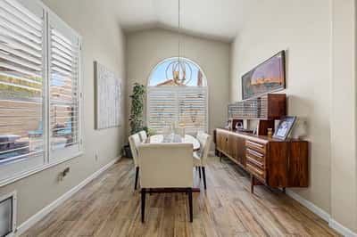 Elegant dining room featuring soaring ceilings, plantation shutters, designer lighting, and beautiful tile flooring. The bright, open atmosphere creates the perfect setting for entertaining family and friends.