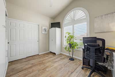 Bright secondary bedroom with vaulted ceilings, plantation shutters, tile flooring, and flexible space for guests, a home office, or creative pursuits.
