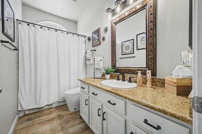 Full guest bathroom showcasing granite countertops, updated hardware, modern lighting, framed mirror, and a convenient tub and shower combination for everyday comfort.