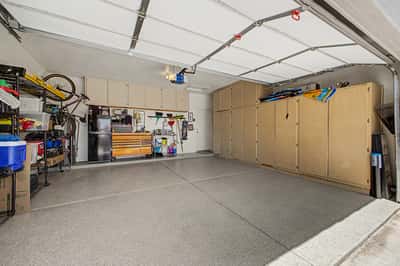 Spacious two-car garage featuring extensive built-in cabinets, epoxy-coated flooring, organized storage, and room for vehicles, tools, and recreational equipment.