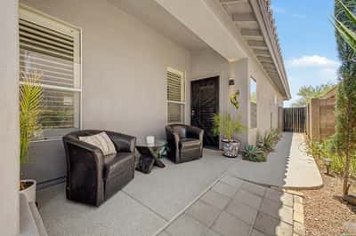 Charming covered side patio featuring comfortable seating, attractive desert landscaping, and secure gated access. This versatile outdoor space offers privacy and additional room to relax in this Mesa home.