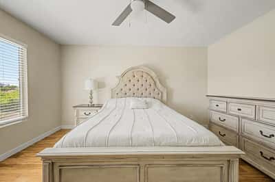 Spacious bedroom offering warm wood-look flooring, abundant natural light, ceiling fan, and flexible living space. A comfortable room designed for everyday functionality.