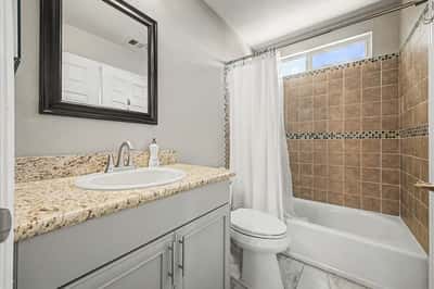 Well-appointed full bathroom featuring granite countertops, decorative tile shower surround, updated cabinetry, and modern finishes. Bright natural light enhances this welcoming Scottsdale space.