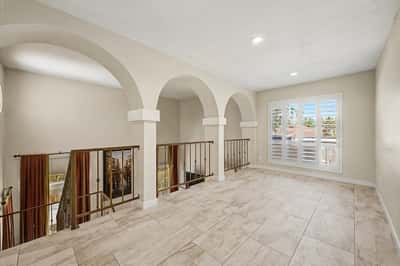 Expansive loft with elegant arches, iron railings, upgraded tile flooring, and an open layout overlooking the main level. A versatile gathering space in this Scottsdale home.