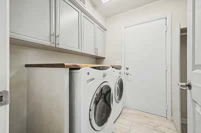 Convenient laundry room with overhead cabinetry, countertop workspace, tile flooring, and space for full-size washer and dryer. Functional storage enhances daily living.