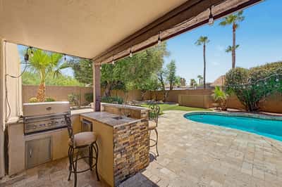 Outdoor entertaining space with a built-in BBQ grill, prep sink, bar seating, covered patio, and views of the sparkling pool. A beautifully designed Scottsdale backyard made for gatherings and outdoor dining.