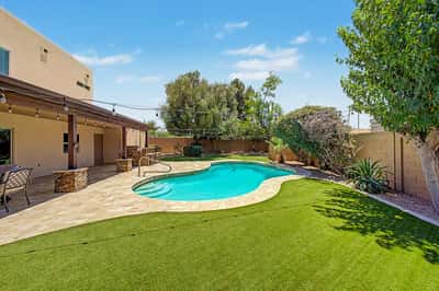 Scenic backyard retreat with a freeform pool, travertine pool deck, lush artificial lawn, and mature landscaping. A private Scottsdale outdoor space perfect for entertaining and everyday enjoyment.