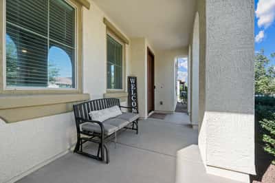 Inviting front entrance featuring a spacious covered patio, decorative columns, and comfortable seating area. Thoughtfully designed to provide shade and curb appeal year-round.