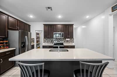 Large quartz island with integrated sink and breakfast bar seating anchors this beautifully appointed kitchen. Rich cabinetry, stainless steel appliances, and a walk-in pantry complete the space.