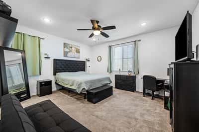 Spacious primary suite with plush carpeting, ceiling fan, generous natural light, and room for additional seating or workspace. A relaxing retreat designed for comfort and privacy in this beautiful Goodyear home.