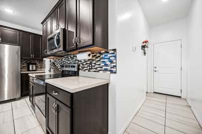 Well-designed kitchen with direct garage entry, modern cabinetry, quartz counters, stainless steel appliances, and decorative backsplash. Convenience and style come together beautifully.