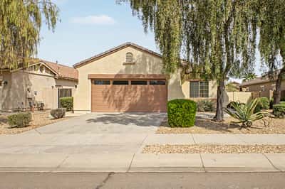 Attractive front elevation showcasing mature trees, low-maintenance landscaping, an attached 2-car garage, and a welcoming entrance in a desirable Goodyear neighborhood.