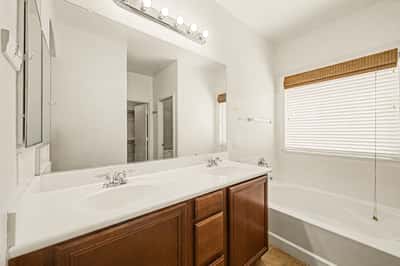 Bright primary bathroom with dual sinks, oversized mirror, abundant cabinetry, soaking tub, and an efficient layout designed for everyday convenience.