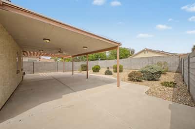 Large covered patio with ceiling fan, extended concrete surface, and views of the beautifully landscaped backyard, providing comfortable outdoor living space in this Goodyear home.