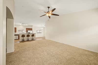 Comfortable living room featuring vaulted ceilings, ceiling fan, plush carpeting, and an open floor plan that enhances the home's bright and airy atmosphere.