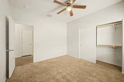 Bright guest bedroom with ceiling fan, neutral d cor, plush carpeting, and generous closet space, ideal as a bedroom, office, or hobby room.