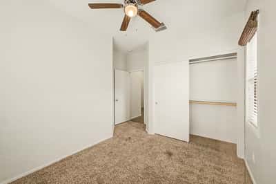 Inviting secondary bedroom with neutral finishes, ceiling fan, plush carpeting, and a roomy closet, providing flexible space for guests, family, or a home office.