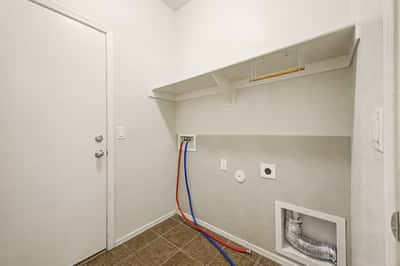 Spacious laundry room featuring tile flooring, washer and dryer connections, built-in shelving, and exterior access for added convenience and organization.
