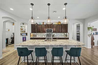Oversized granite island with breakfast seating anchors this upgraded kitchen featuring custom cabinetry, pendant lighting, and an open layout ideal for entertaining and everyday family living.