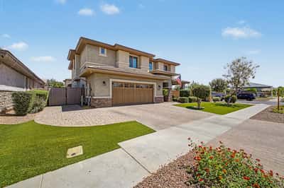 Exterior view highlighting the extended paver driveway, lush landscaping, covered front porch, and attached 3-car garage, creating outstanding curb appeal in Morrison Ranch.
