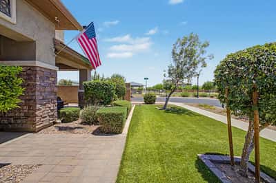 Professionally landscaped front yard with green lawn, mature trees, paver walkway, and inviting curb appeal enhances the beauty of this exceptional Morrison Ranch home in Mesa.