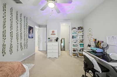 This spacious bedroom includes room for both sleeping and studying, featuring neutral finishes, ceiling fan, plush carpeting, and flexible living space.