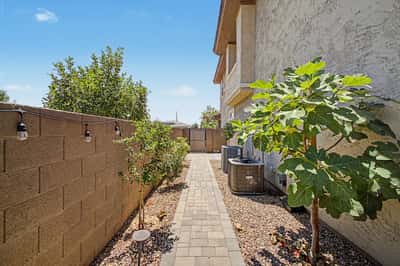 Functional side yard features a paved walkway, mature landscaping, low-maintenance desert design, and secure gated access for added convenience and ease of maintenance.