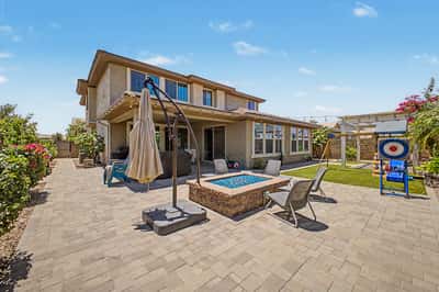 Spacious backyard combines a custom fire feature, expansive paver patio, artificial grass, and covered outdoor living space to create an ideal setting for entertaining.