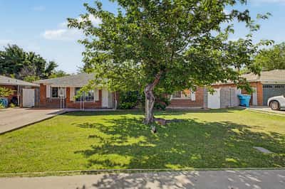 Full front exterior featuring a mature shade tree, lush green lawn, brick construction, and inviting front walkway. This Phoenix home offers timeless curb appeal and attractive outdoor space.