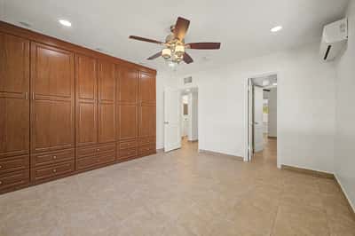 Spacious bedroom offering a full wall of custom built-in wardrobe cabinetry, tile flooring, ceiling fan, recessed lighting, and flexible space ready for your personal design.