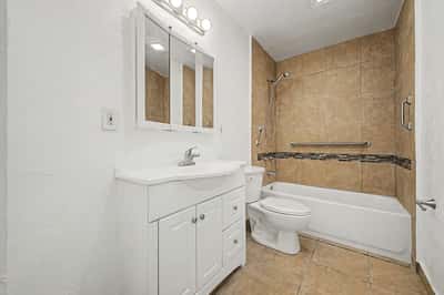 Renovated bathroom with updated vanity, decorative tile surround, grab bars, modern lighting, and durable flooring. The tasteful updates create a bright and functional bathroom within this Phoenix home.