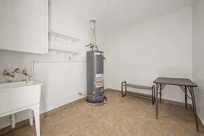 Spacious utility room featuring a utility sink, shelving, water heater, and abundant storage space. Ideal for laundry, organization, and everyday household tasks in this well-maintained Phoenix property.