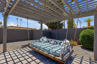 Covered pergola provides a suspended daybed swing, decorative lighting, and a tranquil outdoor lounge area surrounded by low-maintenance landscaping in Scottsdale.