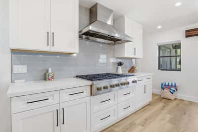 Premium gas range, designer vent hood, quartz counters, and custom cabinetry create a sophisticated cooking space with both style and functionality for home chefs.