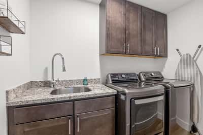 Modern laundry room features a utility sink, granite countertops, overhead cabinetry, and quality appliances, delivering convenience and additional storage for everyday living.
