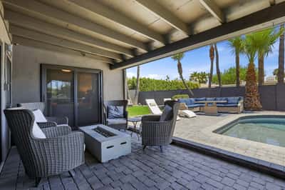 Covered patio overlooks the sparkling pool, fire feature, and professionally designed outdoor entertaining space with paver decking and comfortable seating, completing this exceptional Scottsdale property.
