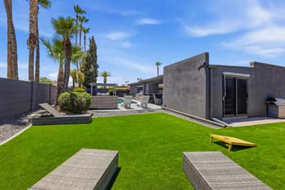Backyard view highlights lush artificial turf, relaxing lounge seating, mature palms, and seamless access to the pool and outdoor living spaces in this Scottsdale home.
