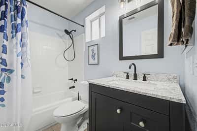 The renovated hall bathroom showcases granite countertops, updated cabinetry, modern black fixtures, stylish lighting, and a tub/shower combination, offering both functionality and contemporary appeal.