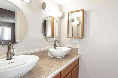 Bright primary bathroom showcases two vessel sinks, generous countertop space, and plentiful cabinetry for convenient daily living.