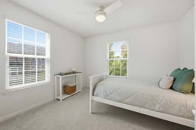 Bright and airy bedroom featuring large windows, modern ceiling fan, and cozy decor for comfort.